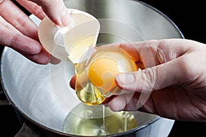 Separating yolk and white of the egg above metal bowl